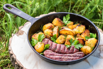 Fried potatoes with meat sausages in a cast-iron frying pan