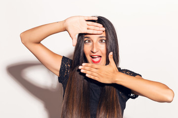 Fototapeta premium Young adult woman framing her face with her hands, making funny faces. In studio over a white background.