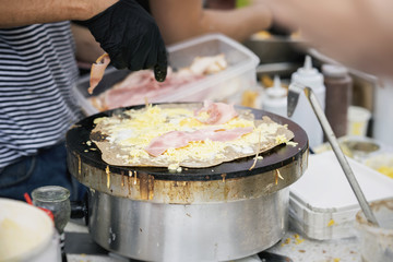 Preparing crepe, galette with ham, cheese and egg on black plate. Cook's hands, summer city party. Concept national food, very tasty fast food, summer party