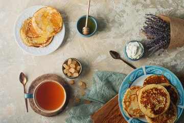 Tea, homemade pancakes, honey, cream sauce and lavender on light concrete table, romantic breakfast pancake party, various morning food, healthy lifestyle. Selective focus, top view