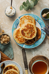 Tea, homemade pancakes, honey, cream sauce and lavender on light concrete table, romantic breakfast pancake party, various morning food, healthy lifestyle. Selective focus, top view