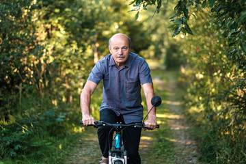 Joyful senior man riding a bike in a park on a beautiful sunny day