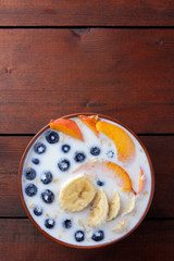 Oatmeal porridge with milk and fruit on a wooden background, healthy porridge with pieces of banana and peach, breakfast with fiber, calcium and vitamins, food for the schoolboy