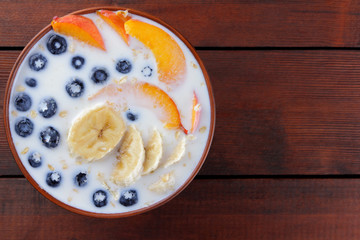 Oatmeal porridge with milk and fruit on a wooden background, healthy porridge with pieces of banana and peach, breakfast with fiber, calcium and vitamins, food for the schoolboy