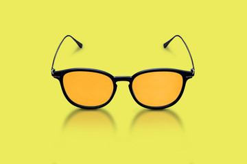 Elegant glasses made of dark plastic and metal, with orange glasses on a yellow background