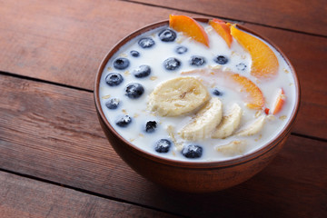 Oatmeal porridge with milk and fruit on a wooden background, healthy porridge with pieces of banana and peach, breakfast with fiber, calcium and vitamins, food for the schoolboy