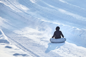 Tubing. Woman or little girl is sliding fast downhill on an inner tube in winter time. Back view