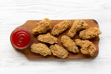 Top view chicken wings on a wooden board with red pepper sauce over white wooden surface. Closeup.