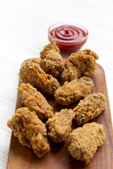 Chicken wings on a wooden board with red pepper sauce on white wooden table, closeup. Selective focus.