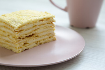 Piece of Napoleon Cake on pink plate over white wooden surface, closeup. Side view.