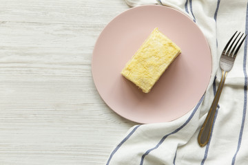 Piece of Napoleon Cake on pink plate over white wooden table, top view. Copy space.