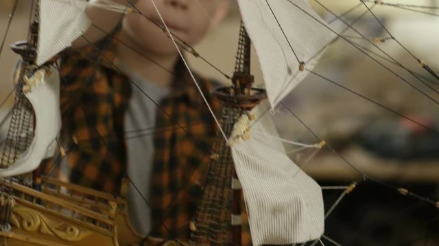 Tilt up of cute schoolboy with paintbrush staining finished ship model