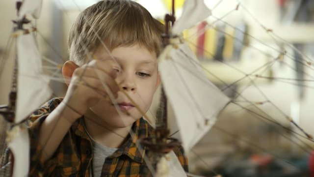 PAN of cute focused little boy with paintbrush staining finished ship model