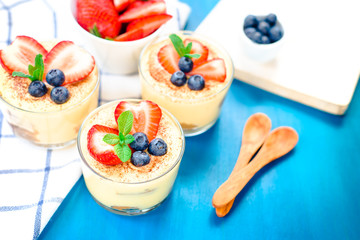 homemade, exquisite dessert tiramisu in glasses decorated with strawberry, blueberry, mint on blue wooden table