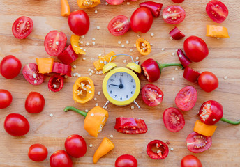 yellow and red peppers, tomatoes with alarm clock on wooden table. Above view