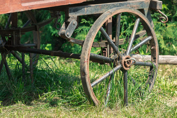 Obraz premium Close up of a wheel in a rusty metal rim from the old wooden cart. The cart costs on the street in the summer on a green grass per sunny day