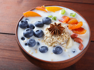 Oatmeal porridge with milk, fruits and peanuts on wooden background, healthy porridge with banana and peach slices, breakfast with fiber, calcium and vitamins, anise, dried apricots in milk