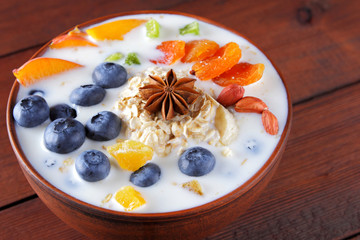 Oatmeal porridge with milk, fruits and peanuts on wooden background, healthy porridge with banana and peach slices, breakfast with fiber, calcium and vitamins, anise, dried apricots in milk