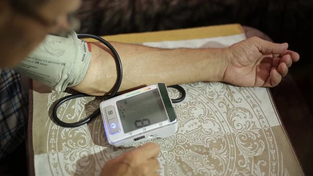 Elderly man measuring blood pressure. An old man sitting in his house at the table. 4k, slow motion. copy space