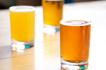 Glass of pale ale on a wood table, with flight of beer tasters in the background