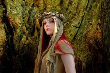 Portraits of a semi-nude woman posing inside a large  hollow oak tree. She is dressed only with rags around her head and wears a thorn wreath on her head. The woman  is seen semi-nude in the photo.