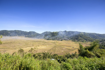 Fototapeta premium Smoke rising above the spider rice fields during harvest time in Flores, Indonesia.