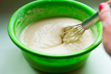 Stir the dough for pancakes. Dough for baking in a green bowl.