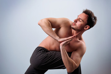 Calm peaceful young bearded Caucasian yoga instructor posing shirtless and barefooted in white...