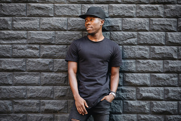 Handsome african american man in blank black t-shirt standing against brick wall - 216902560