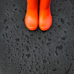 The edges of the orange rain boots are on a wet wet surface covered with raindrops. Top view, copy...