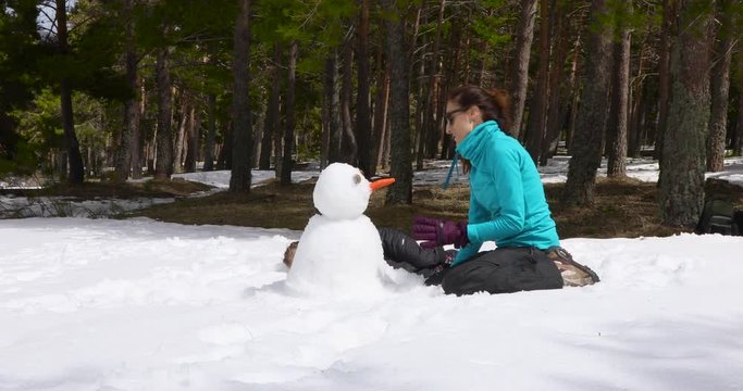 Happy family. Woman mother and four years old blonde child, sitting on their knees, playing with snow to make a sculpture in winter nature. 4k video. 
