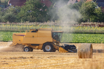 M&auml;hdrescher bei der Kornernte mit Strohballen auf einem Stoppelfeld im Vordergrund