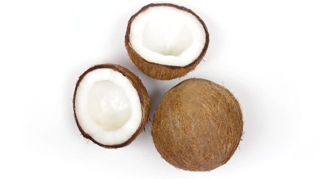 Top view of one whole ripe brown tropical coconut and two halves with yummy white pulp rotating on white isolated background. Healthy fresh tropical fruits. Loopable seamless cocos rotating