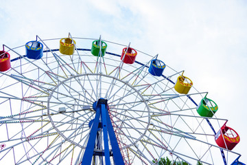 Large and bright ferris wheel against a clear blue sky. Long spokes and multi-colored seats. Concept of joy and good mood