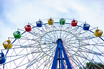 Large and bright ferris wheel against a clear blue sky. Long spokes and multi-colored seats. Concept of joy and good mood