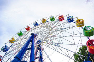 Large and bright ferris wheel against a clear blue sky. Long spokes and multi-colored seats. Concept of joy and good mood