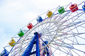 Large and bright ferris wheel against a clear blue sky. Long spokes and multi-colored seats. Concept of joy and good mood