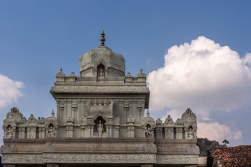 Obraz premium Shravanabelagola, Karnataka, India - November 1, 2013: Gray cement upper structure of gate into the Jain sanctuary features dome and small statues under blue sky with white cloud.