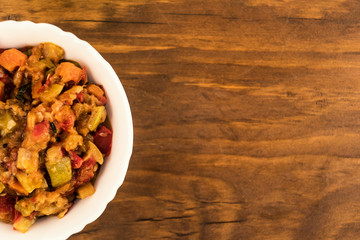 Cold vegetarian appetizer of squash caviar with tomatoes, carrots, onions and sweet pepper in a porcelain plate on a wooden background, top view.