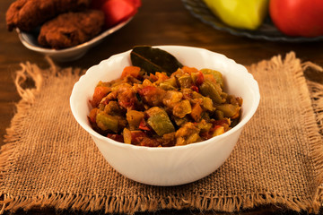 Appetizer of sliced stewed zucchini and tomatoes with carrots, sweet pepper and onions, laid in a porcelain plate with Bay leaf.
