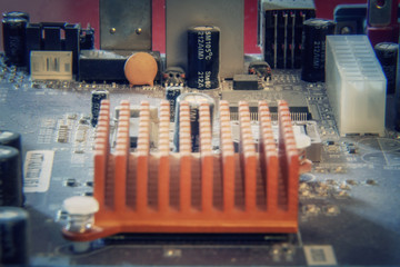 A landscape made of computer components on a motherboard, focus on an orange dissipator. Above...
