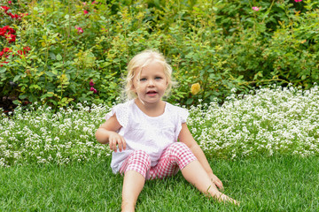 Cute little girl sitting in the grass in the garden