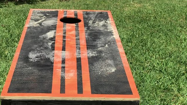 Beanbags landing on home made cornhole game with dust flying