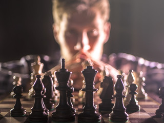 young bearded chess player playing a game on a tournament with dark background