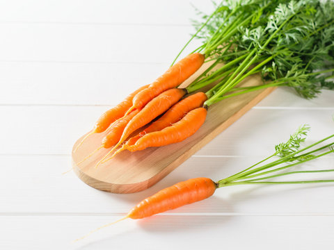 A bunch of fresh carrots on a chopping Board and one carrot on a white wooden table.