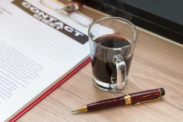 Pen,black coffee,business document and contact sheet with warm morning light near the window.Copy space.