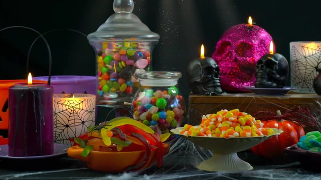 Happy Halloween trick or treat party table with bowls and apothecary jars of candy with skull candles against a black background, scooping candy close up.