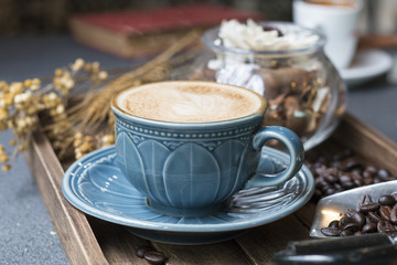 Latte cup,coffee bean,book and dried flowers jar on wooden tray with warm morning light near the window.Copy space.