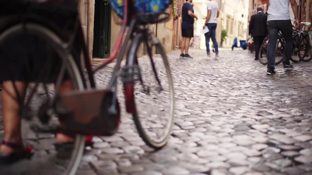Italian lifestyle and Italian culture. An old Italian woman goes out of the market with products that carry their bike on the trunk. It runs along narrow streets with a pavement. Around her are people