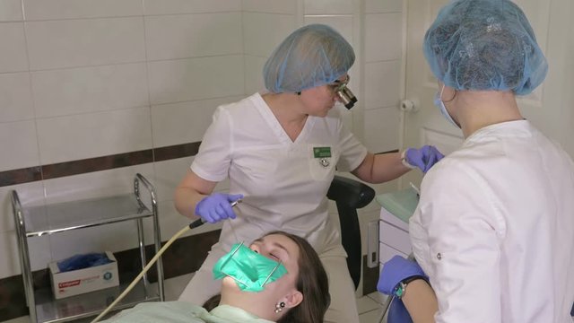 Woman at dentist clinic gets dental treatment to fill a cavity in a tooth. Dental restoration and composite material polymerization with UV light and laser. The doctor works with an assistant.